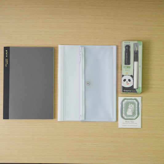 plain black daigo isshoni. notebook, a white daigo pvc cover, and a black capped, white bodied panda pilot kakuno with swatch cards bundle on a desk.
