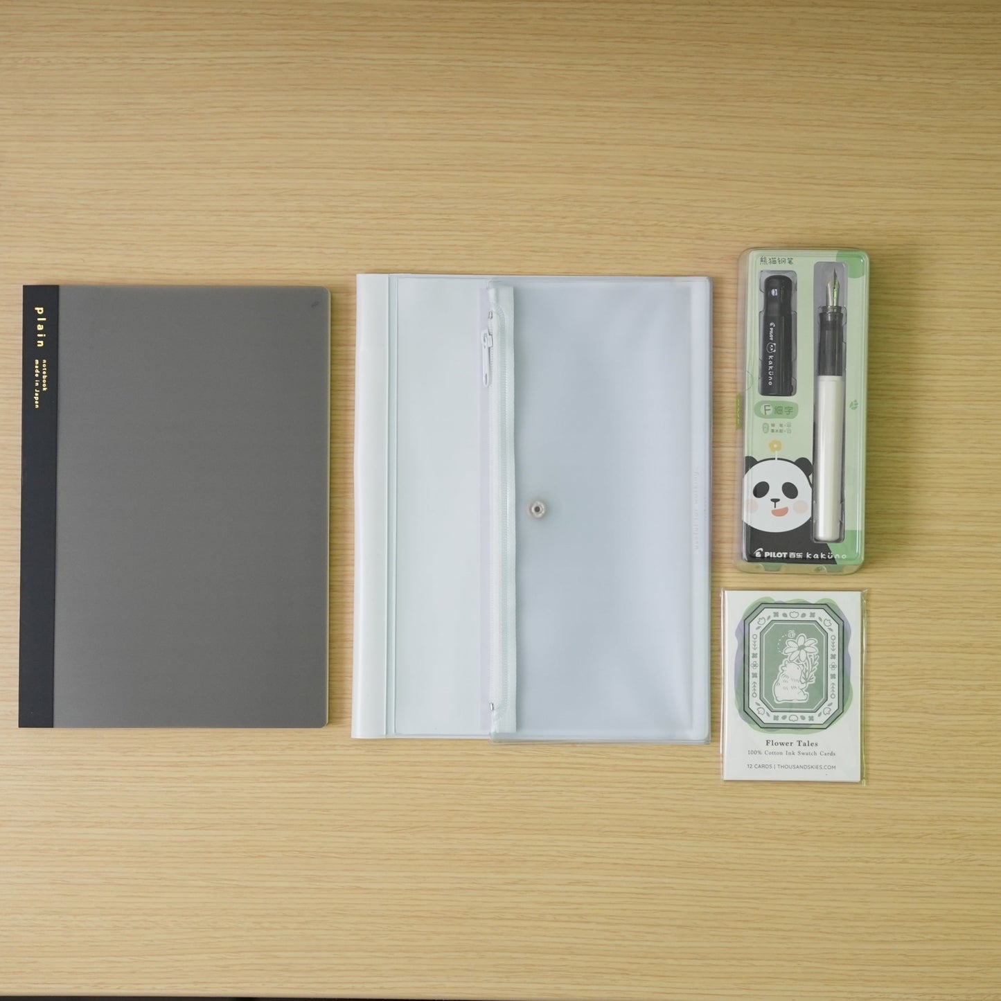 plain black daigo isshoni. notebook, a white daigo pvc cover, and a black capped, white bodied panda pilot kakuno with swatch cards bundle on a desk. 