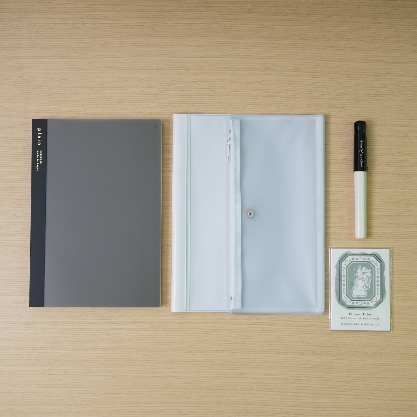 plain black daigo isshoni. notebook, a white daigo pvc cover, and a black capped, white bodied panda pilot kakuno with swatch cards bundle on a desk. 