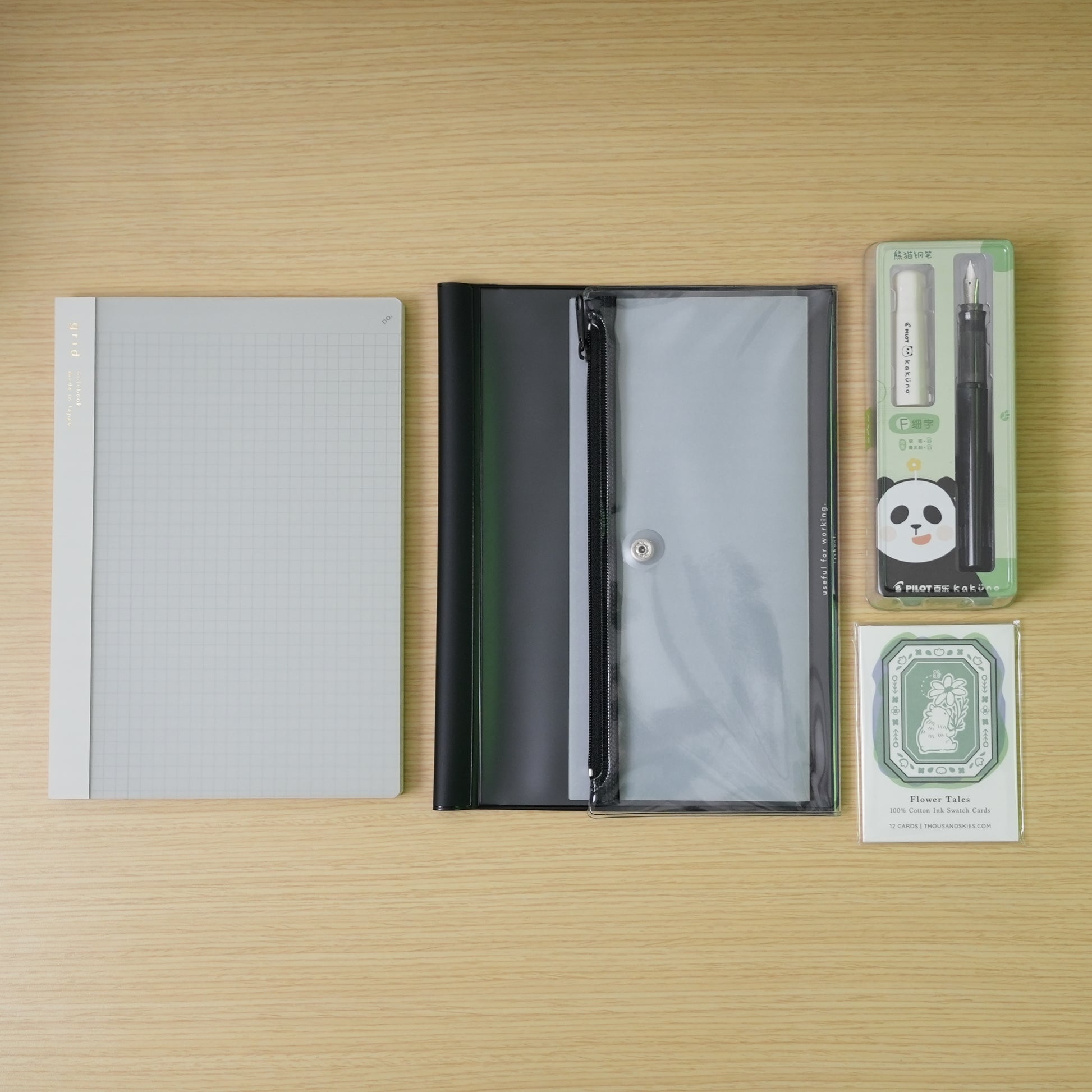 plain white daigo isshoni. notebook, a black daigo pvc cover, and a white capped, black bodied panda pilot kakuno with swatch cards bundle on a desk. 