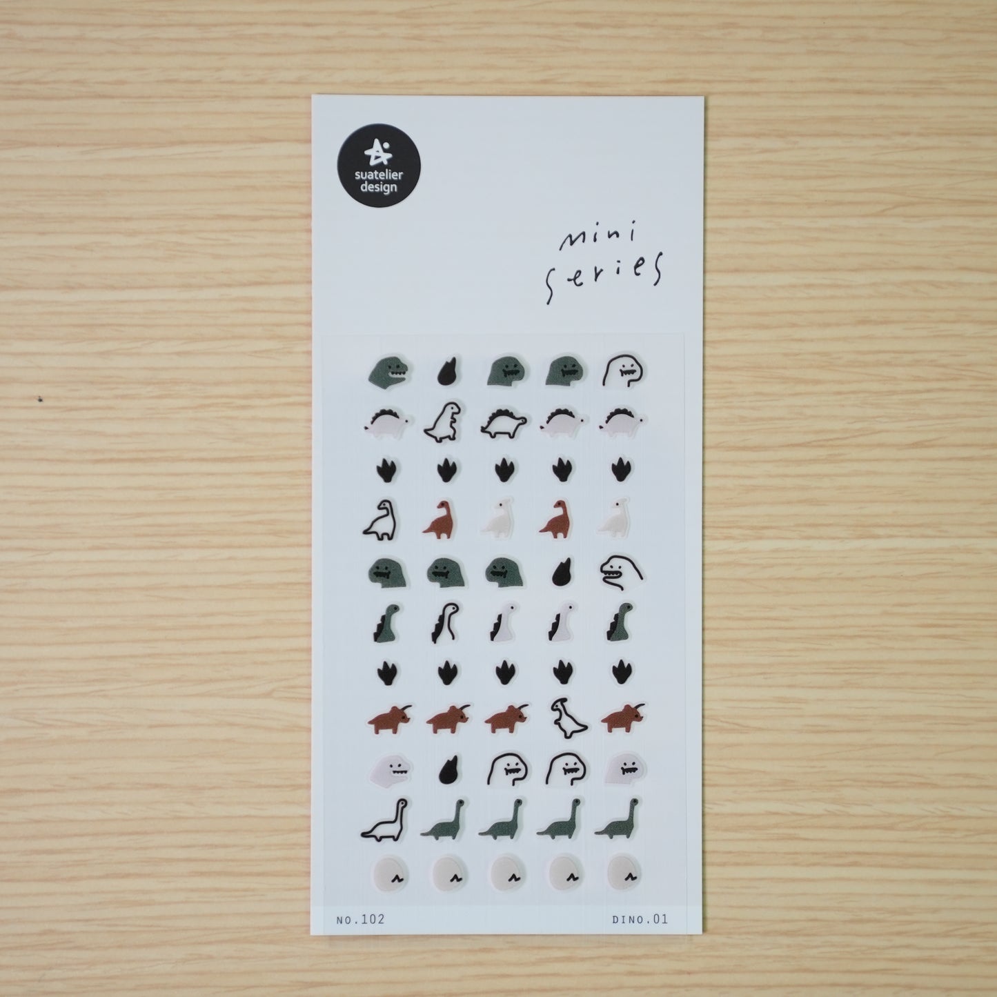 Suatelier mini PVC dinosaur stickers shown individually — stegosaurus, drop, long-neck, and ghost dino on wood desk