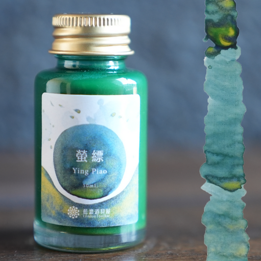 Lennon Tool Bar Ying Piao bottle on a wooden desk next to a swatch for it.  A green ink with yellow shading and hold and green shimmer. 